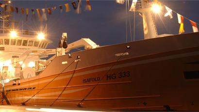 Fiskebåd ISAROLD HG-363 med flag og lys om natten ved havnen.