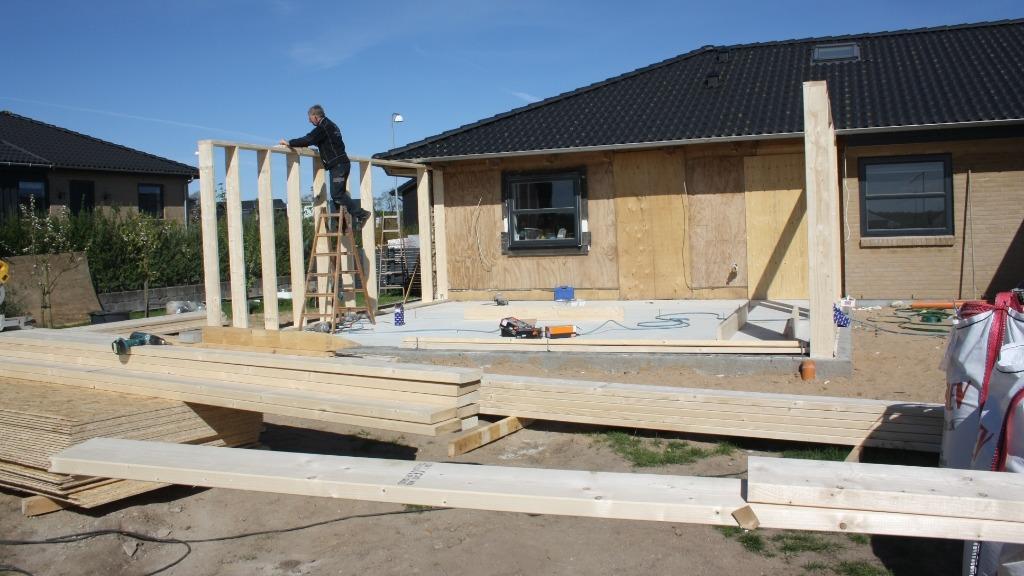 Byggeri af et hus med træstolper og en håndværker på en stige, der arbejder på væggen.