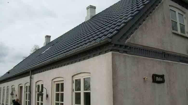 Et hus med blå tag og hvid facade, set fra en vinkel, med flere vinduer og skorsten.