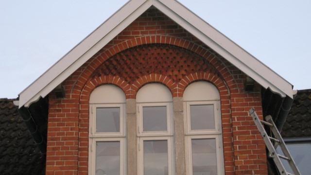 Tagvindue i murstensbygning med buede detaljer og stige ved siden af.