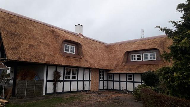 Et charmerende hus med stråtag og sort-hvide bindingsværk, beliggende i en grøn have.