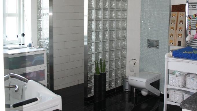 Moderne badeværelse med glasblokke, badekar, toilet og sorte fliser.
