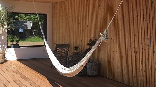Hængekøje hængende i en moderne terrasse med trævæg og planter i baggrunden.