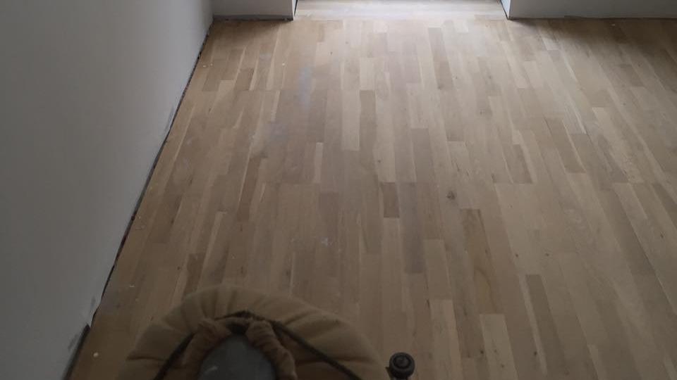 Billede af et rum med lyst trægulv og en døråbning til et andet rum.