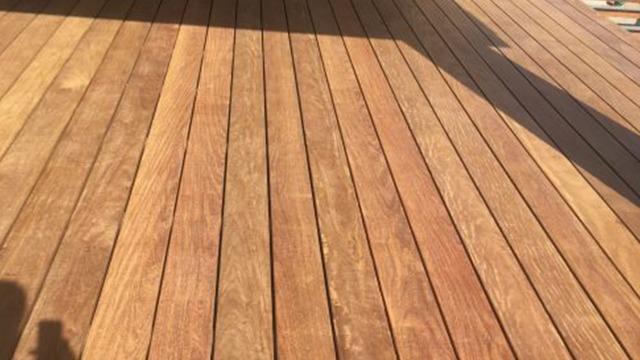 Et tæt billede af en ny træterrasse med glatte, varme træplanker i forskellige nuancer af brun.