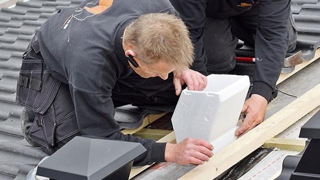 To håndværkere arbejder på et tag, mens de installerer en hvid tagventilation.