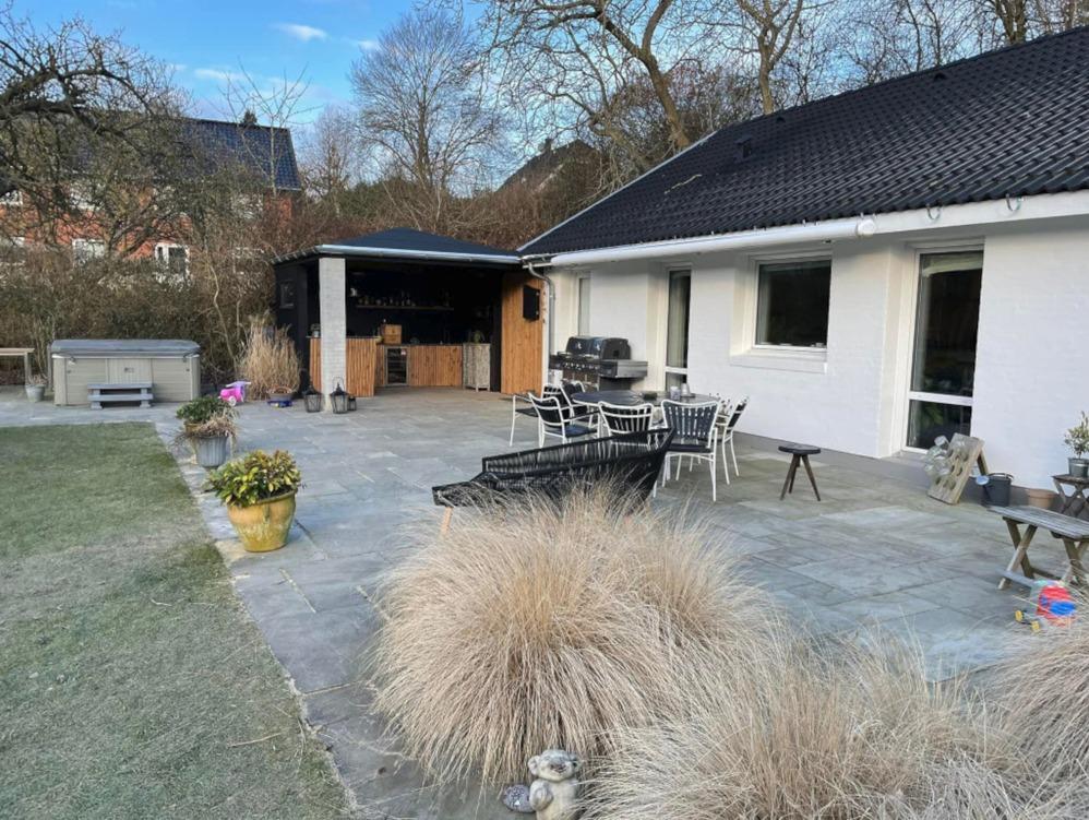 Hus med terrasse og udendørs spiseplads, omgivet af planter og græs, i et roligt område.