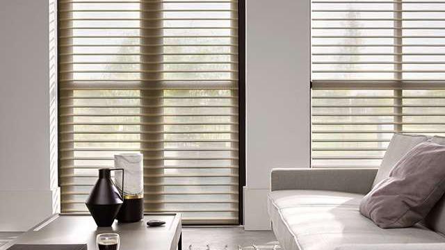 Moderne stue med persienner, sofa og dekorative genstande på bordet. Lys strømmer ind gennem vinduerne.