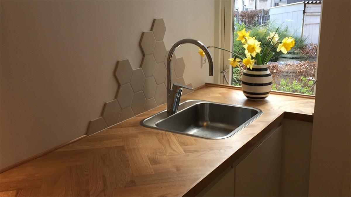 Moderne køkken med en stålvask, træbordplade og en vase med påskeliljer ved vinduet.