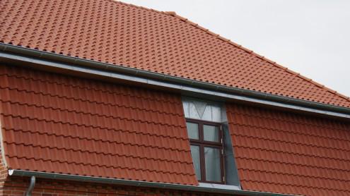 Tag med røde teglsten og et vindue i en murstensbygning under en grå himmel.