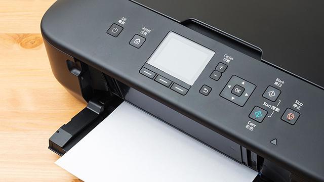 En printer med kontrolpanel og et papir, der er ved at blive udskrevet, på en træoverflade.