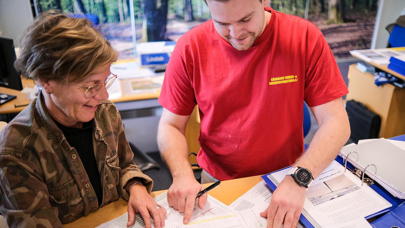 To personer, en mand og en kvinde, arbejder sammen om dokumenter ved et skrivebord i et kontormiljø.