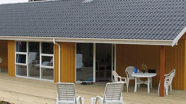 Moderne hus med orange facade og grå tag, terrasse med hvide havemøbler og bord.
