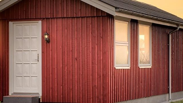 Rødt træhus med hvid dør og vinduer, belyst af solnedgangen.