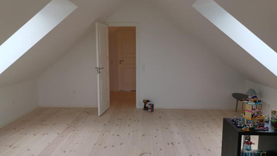 Lyst værelse med skrå vægge, åbne døre og en lille reol med legetøj i hjørnet.
