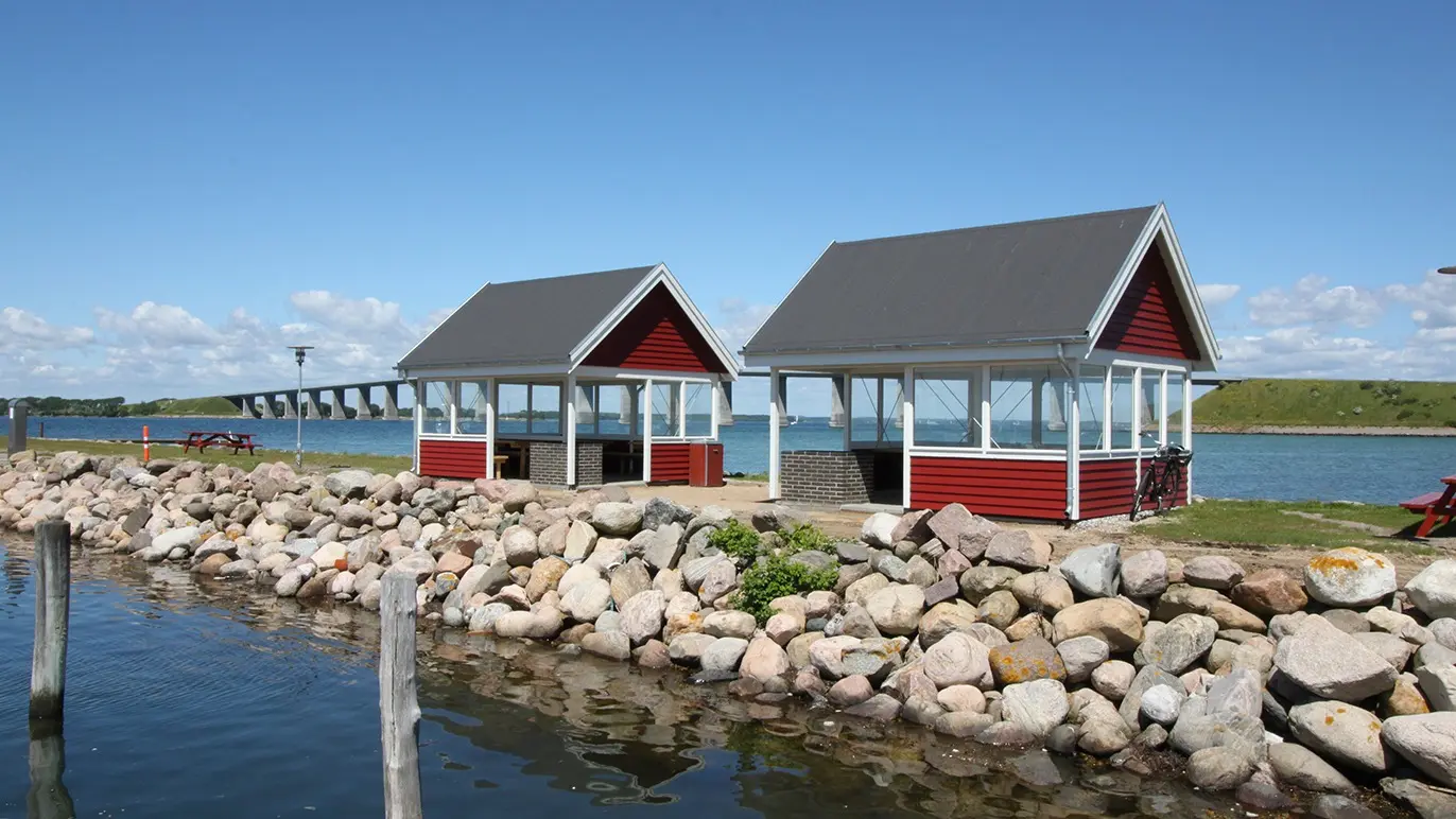 To små røde pavilloner ved vandet, omgivet af store sten og en klar blå himmel.