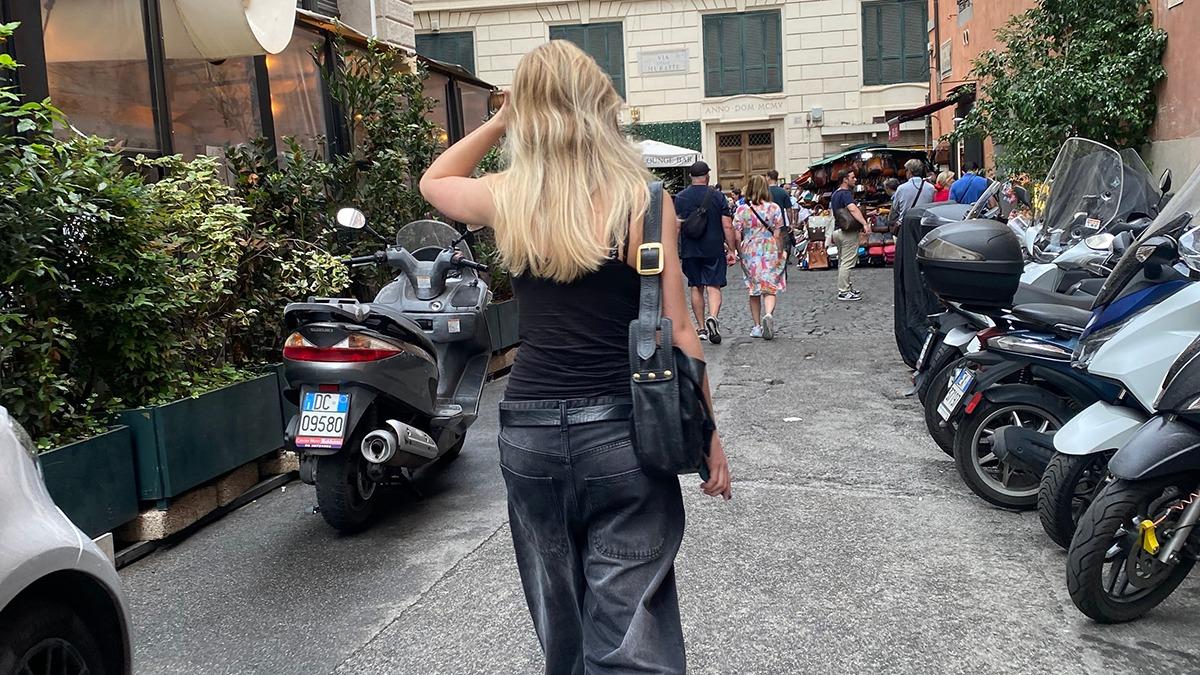 En kvinde med langt hår går gennem en smal gade fyldt med motorcykler og mennesker i en livlig atmosfære.
