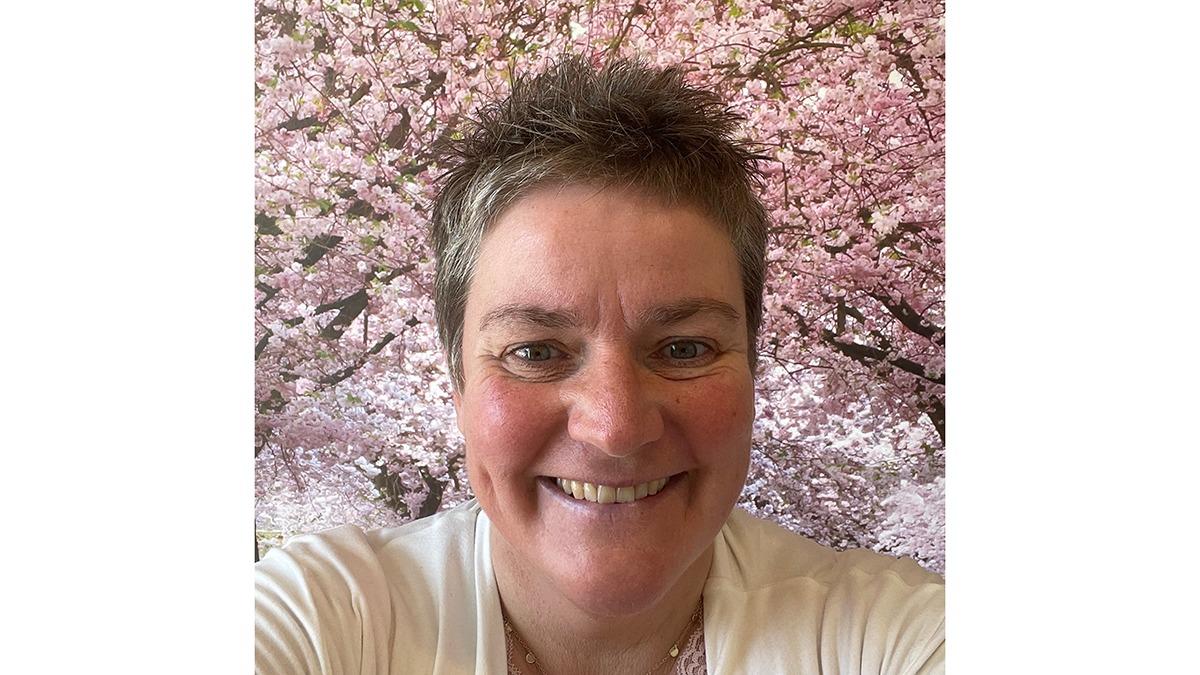 Kvinde smiler foran en baggrund med blomstrende kirsebærtræer.