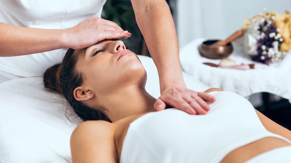 En kvinde får en afslappende ansigtsmassage på en behandlingsbriks med en behandler ved siden af.