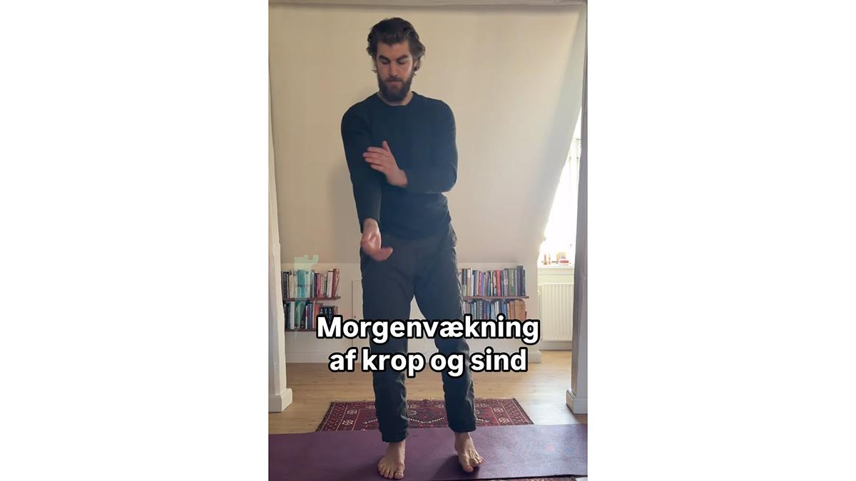 Mand står på en yogamåtte og udfører morgenøvelser for krop og sind i et lyst rum.