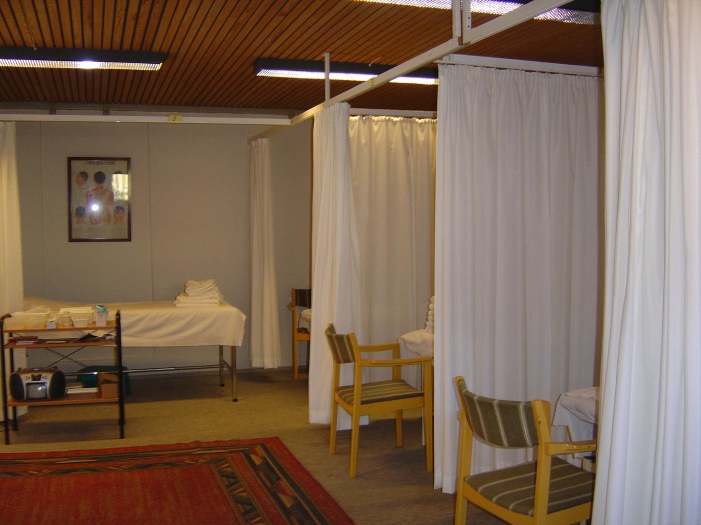 Et værelse med adskilte senge og stole, dækket af hvide gardiner, i en klinisk indretning.