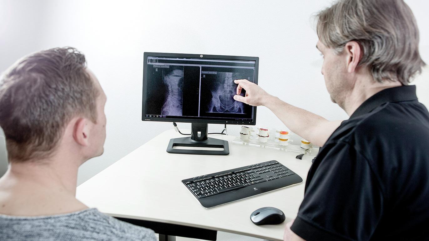 Læge viser patient røntgenbilleder på en computerskærm under en konsultation.