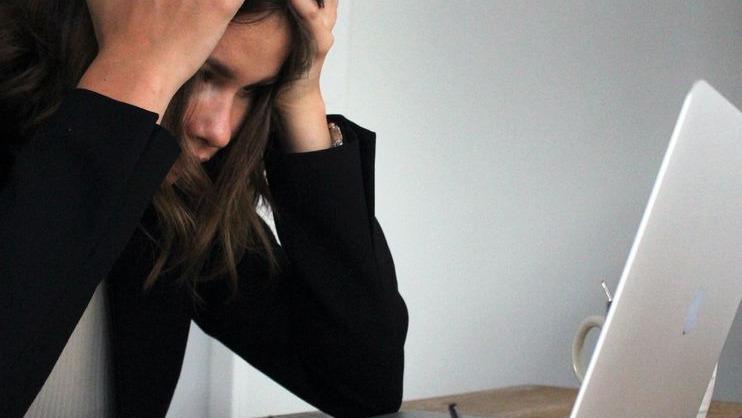 En kvinde sidder ved en computer med hænderne i håret, ser stresset og frustreret ud.