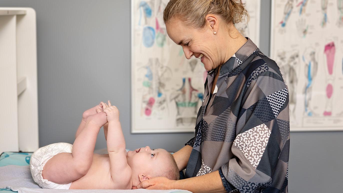 En glad mor leger med sin baby, der ligger på skiftetabel, mens de smiler til hinanden.