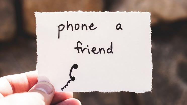 En hånd holder et papir med teksten "phone a friend" og en tegning af en telefon.