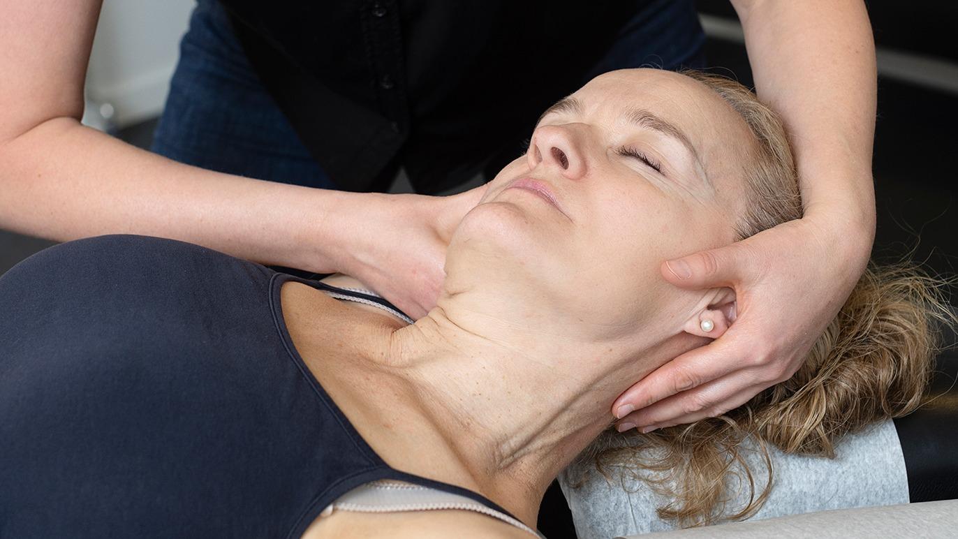 Kvinde får nakkemassage af behandler, der holder hendes hoved og nakke under behandlingen.