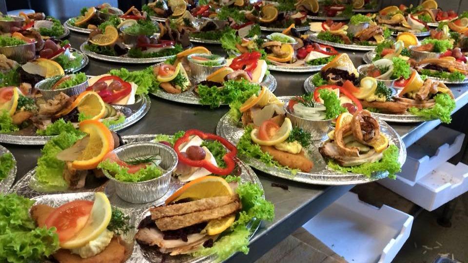 Flere tallerkener med farverige sandwiches, salat, grøntsager og citronskiver anrettet til servering.