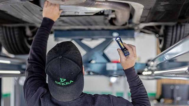 Mekaniker arbejder under en bil med en lommelygte i et autoværksted.