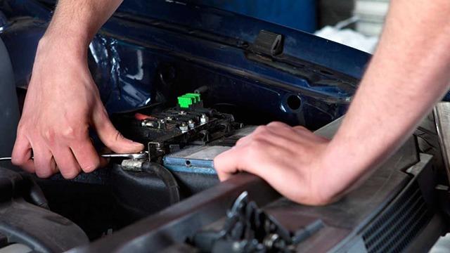 En mekaniker arbejder på bilbatteriet med en skruenøgle i et værksted.