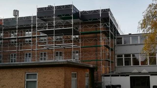 Bygning med stillads omkring, der viser renovering af murværk og tagarbejde.