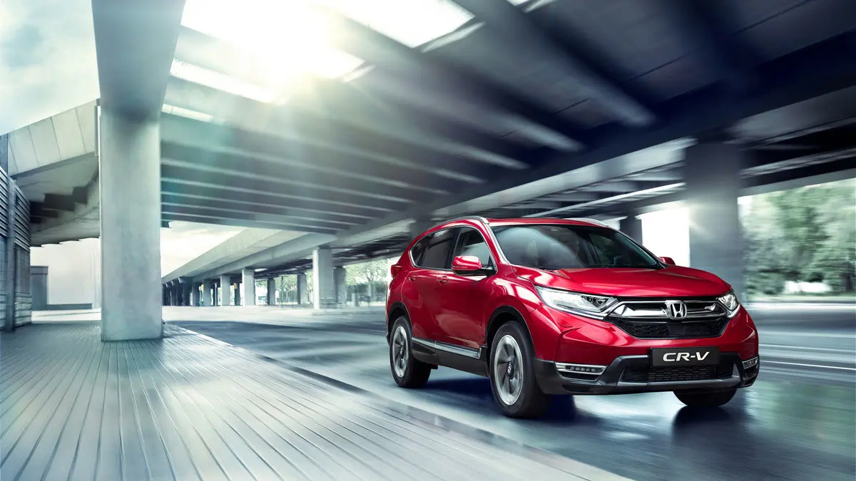 En rød Honda CR-V kører på en moderne vej under en bro med lysstråler, der skinner ned.