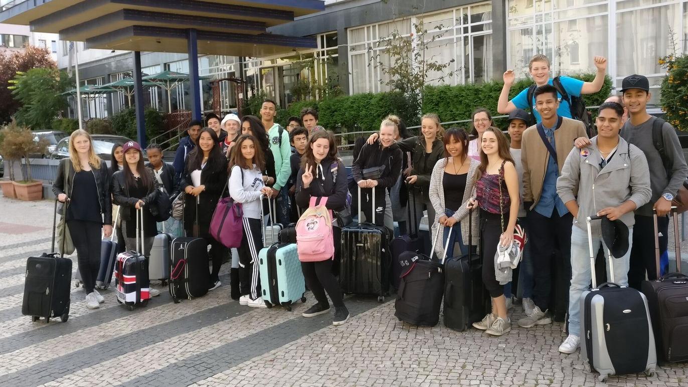 Gruppe af unge mennesker med kufferter foran en bygning, klar til at rejse.