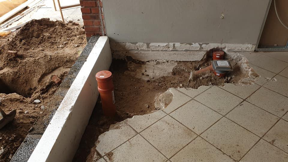 Billede af en byggeplads med en ujævn gulvflade, synlige rør og sand i hjørnet af rummet.