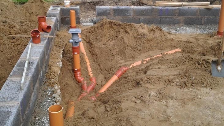 Rørinstallation i en byggegrav med sand og mursten, klar til fundamentarbejde.