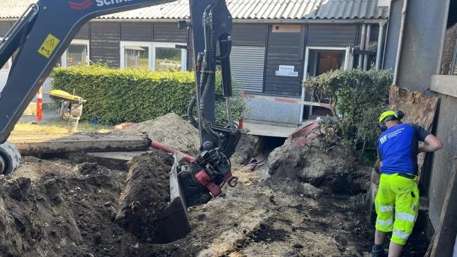 Gravemaskine arbejder på en byggeplads, mens en arbejder står ved en væg og overvåger processen.