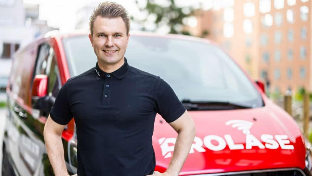 En smilende mand i sort polo t-shirt står foran en rød varevogn med logoet "Prolase".