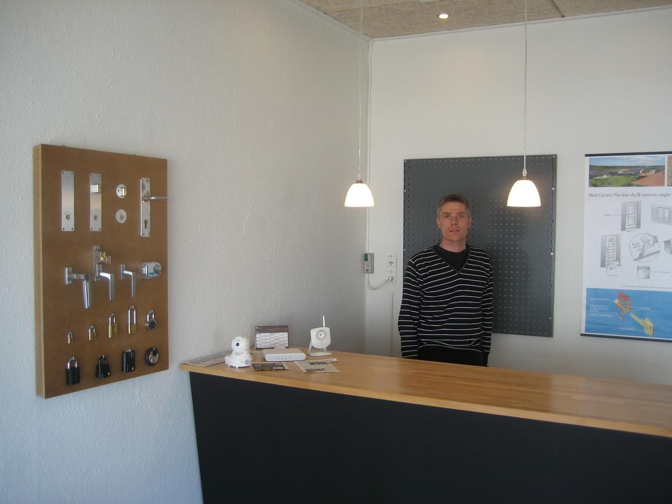 En mand står bag en reception med en træplade og forskellige dørgreb på væggen.
