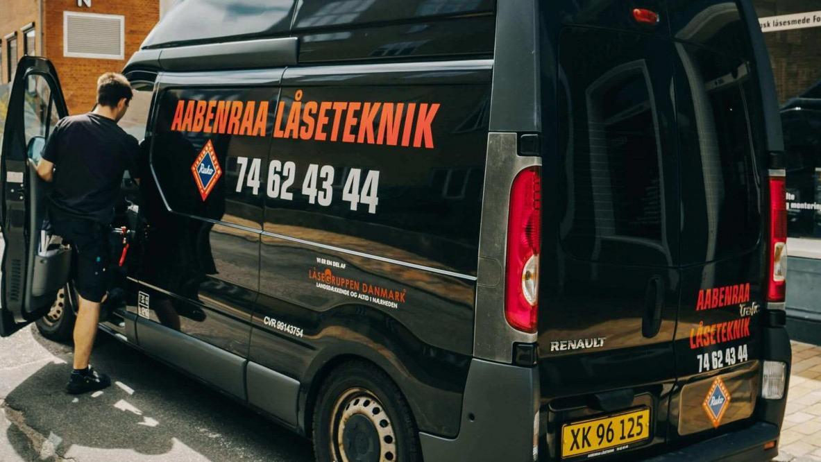 En mand åbner døren til en sort varevogn med teksten "Aabenraa Låseteknik" og kontaktinformation.