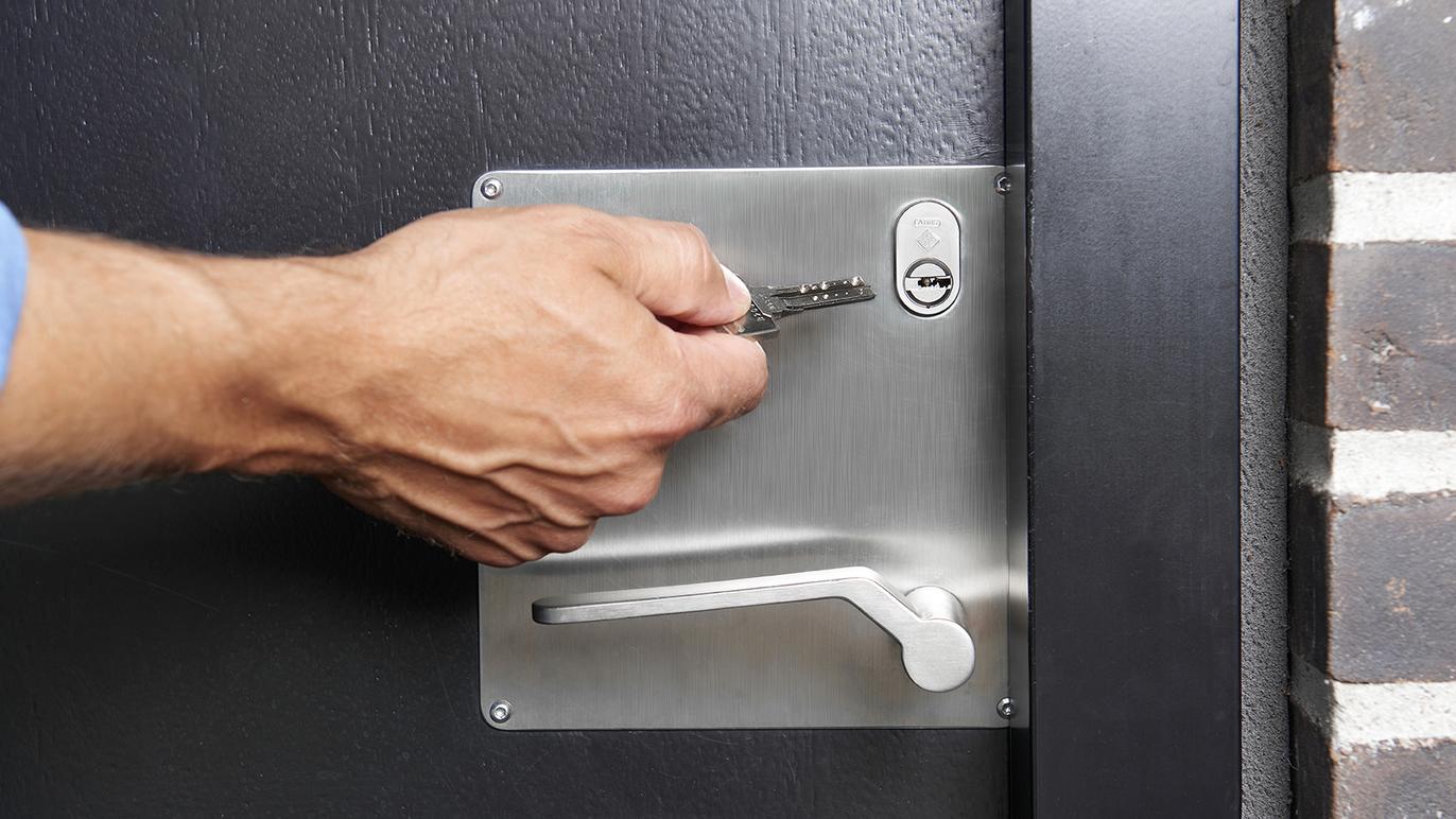 En hånd, der indsætter en nøgle i en lås på en sort dør med metalbeslag.