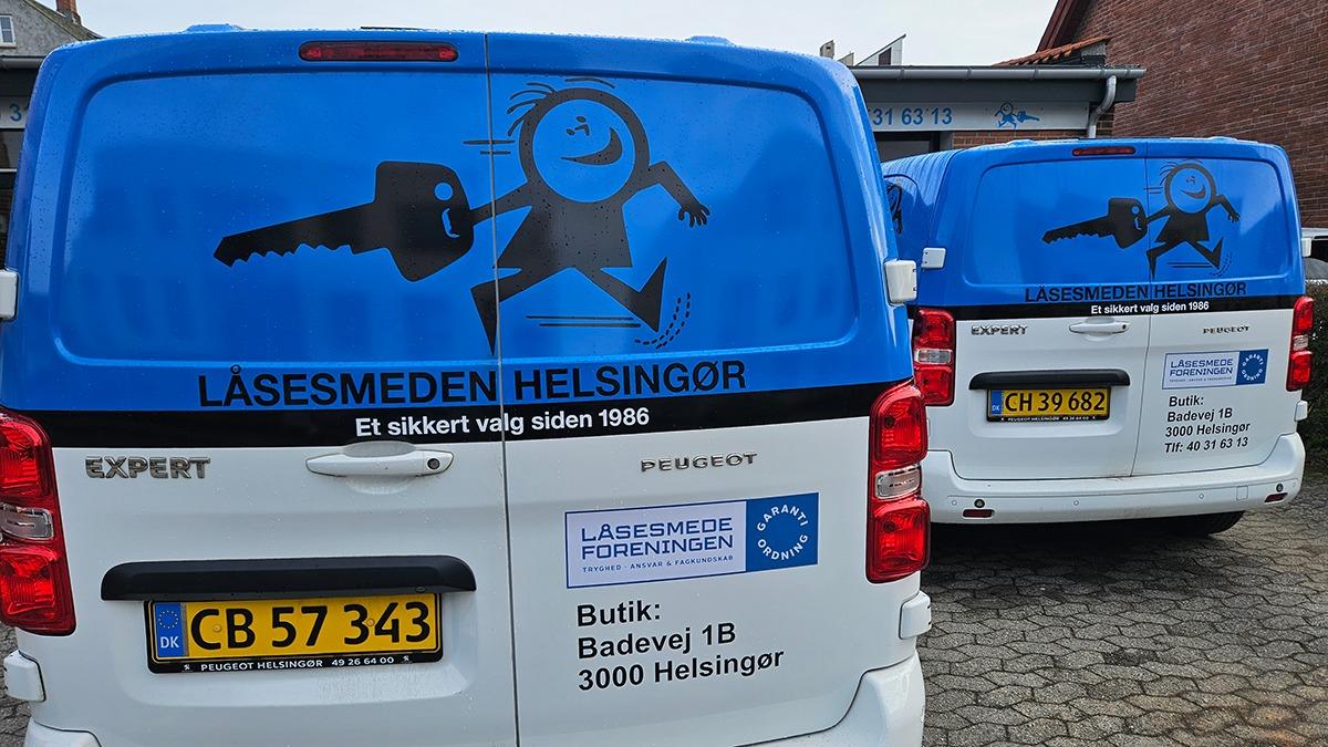 Biler med reklame for Låsesmeden Helsingør, der viser en nøgle og en glad figur på bagsiden.