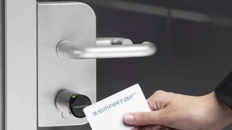 En hånd holder et adgangskort, der scannes ved en moderne dør med et Smartair-låsesystem.