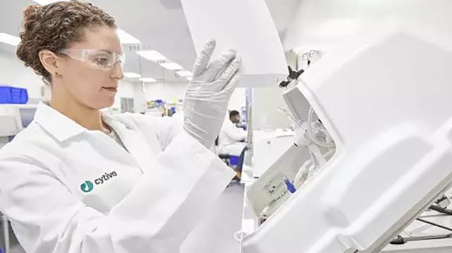En kvinde i laboratoriefrakke arbejder med en maskine i et moderne laboratorium. Hun bærer beskyttelsesbriller og handsker.
