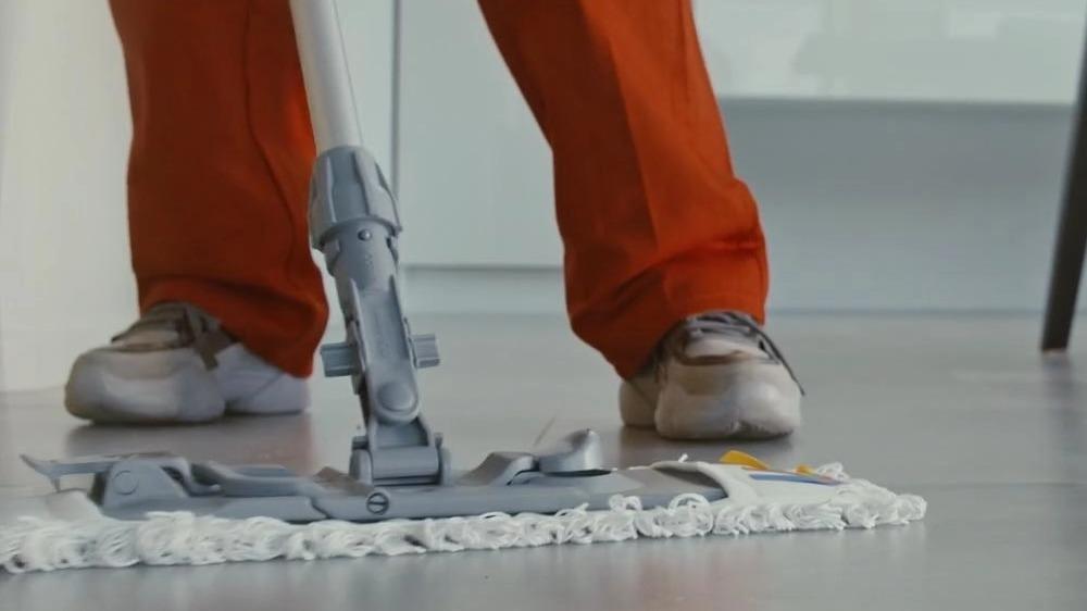 En person i orange bukser og sneakers, der bruger en moppe til at rengøre et lyst gulv.