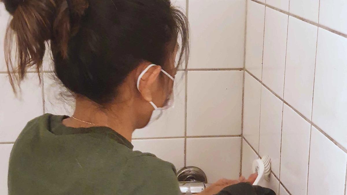En person med en maske står ved en væg og tilslutter en elektrisk enhed i et badeværelse.