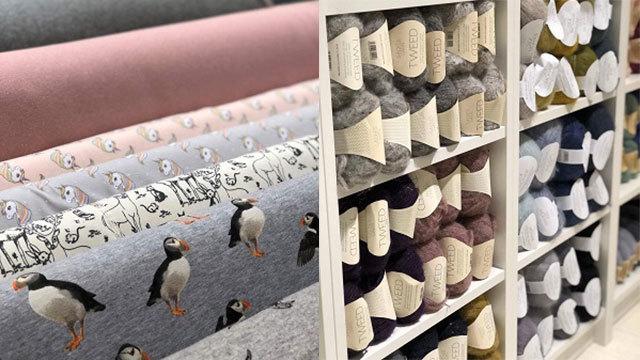Ruller af stof med forskellige mønstre og garnnøgler i en butik, herunder fuglemønstre og bløde farver.