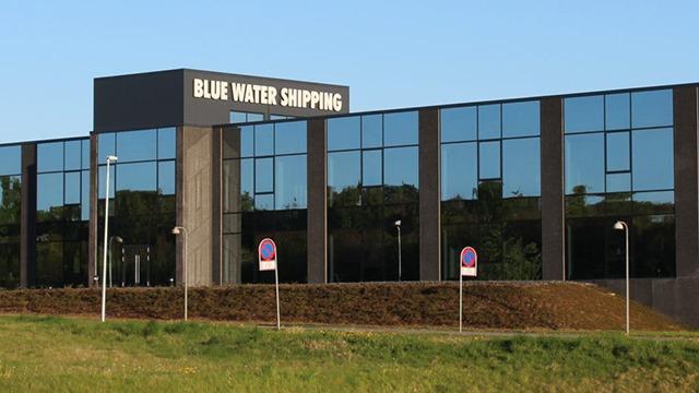 Moderne kontorbygning med skiltet "Blue Water Shipping" og store vinduer i dagslys.
